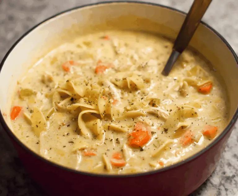 A steaming bowl of creamy chicken noodle soup garnished with fresh herbs, featuring tender chicken, hearty noodles, and a rich, flavorful broth.