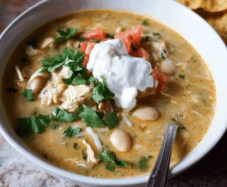 Creamy white bean enchilada soup topped with shredded cheese, fresh cilantro, and sliced jalapeños in a bowl garnished with lime wedge, served with tortilla chips.