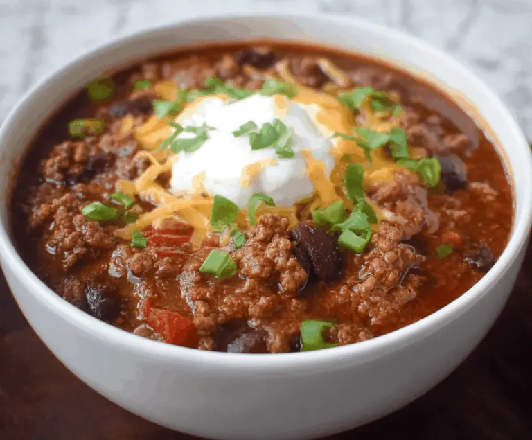 A bowl of flavorful ground beef stovetop chili garnished with chopped cilantro and shredded cheese, served with a side of corn tortilla chips.