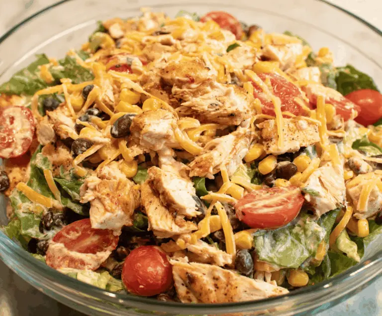 Colorful Southwest Chicken Salad featuring grilled chicken, fresh lettuce, cherry tomatoes, black beans, corn, avocado slices, shredded cheese, and a tangy dressing in a vibrant bowl.