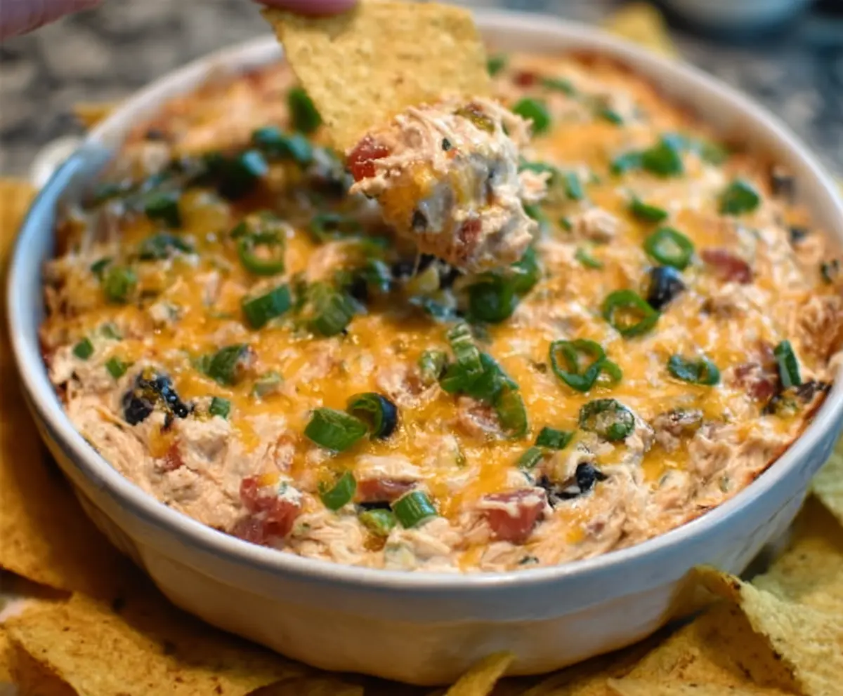 Creamy chicken taco dip with melted cheese, fresh tomatoes, and cilantro in a serving bowl.