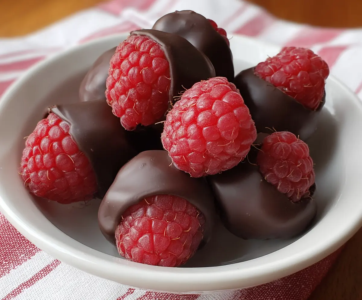 Delicious chocolate-covered raspberries on a white plate, perfect for a sweet treat or dessert decoration.